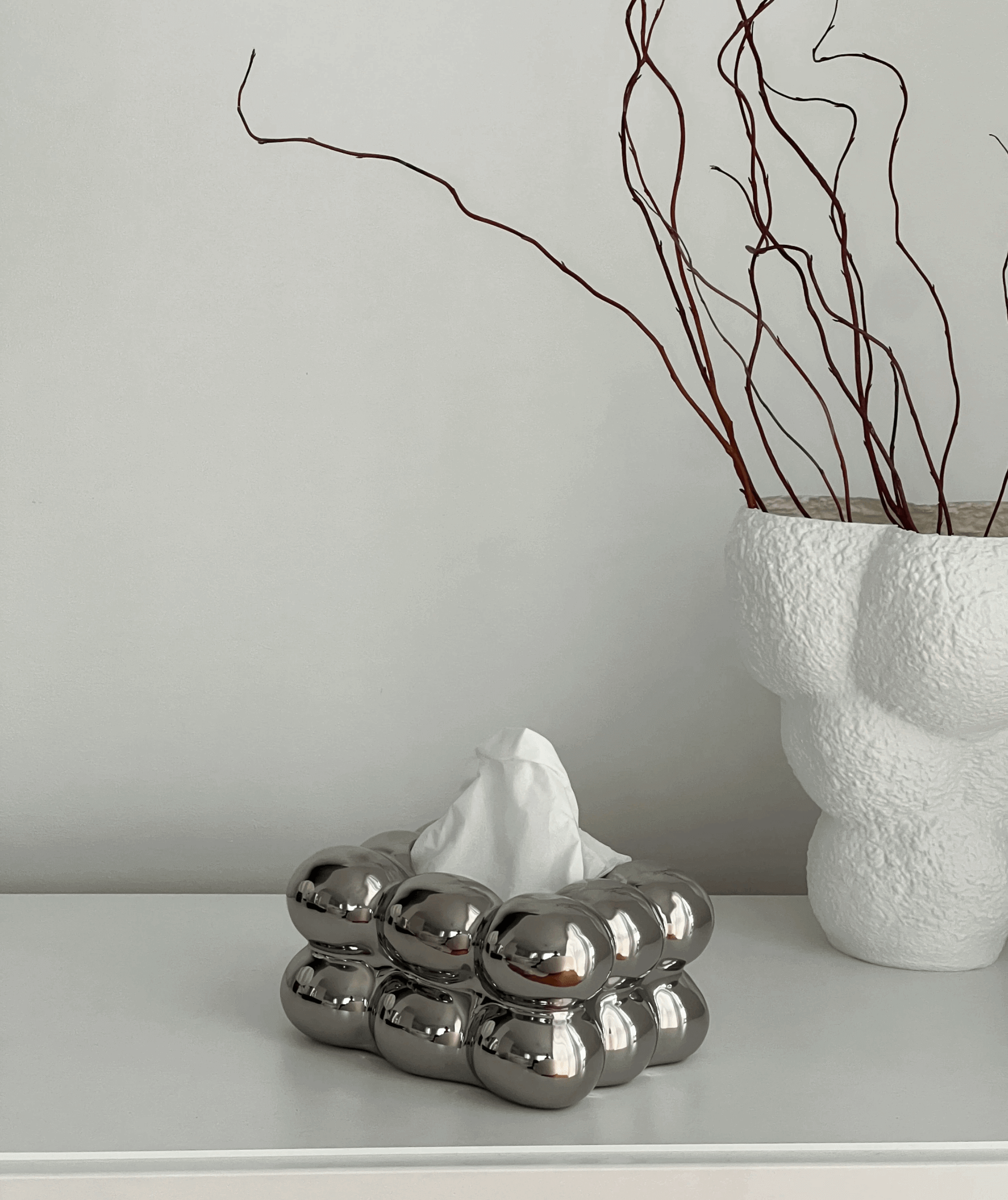 Luxurious ceramic bubble tissue box with a modern design on a white surface, next to a minimalist vase with branches.